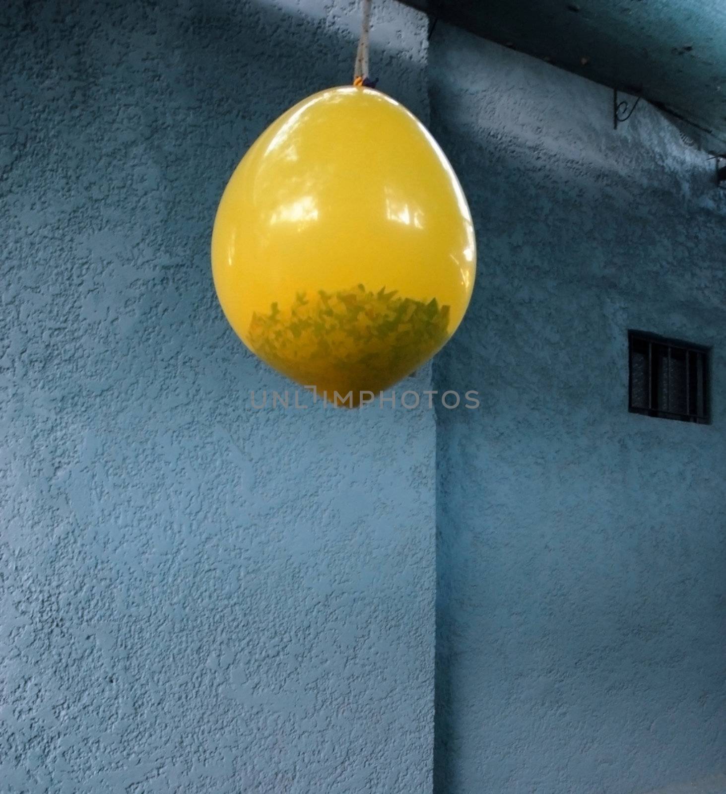 Pinata. Hanging yellow balloon with gifts and confetti inside. Rough wall texture background
