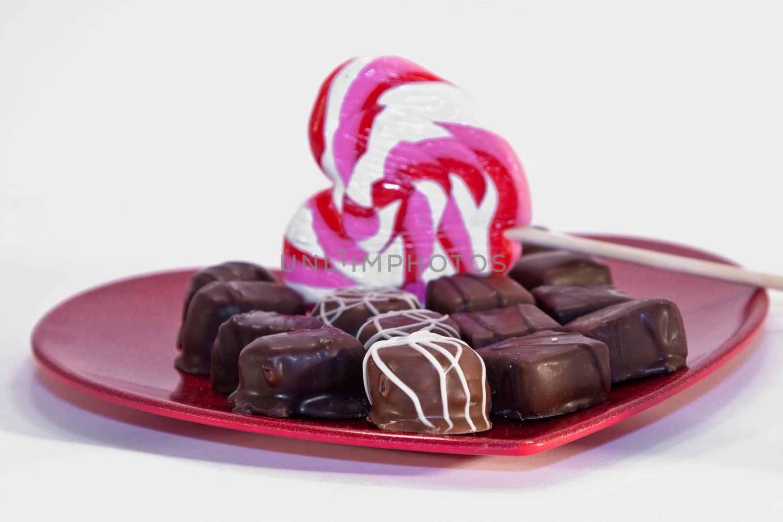 A variety of chocolates with a heart shaped lollipop on a red metallic heart plate isolated on white