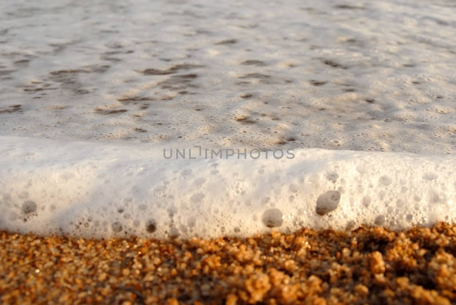 Wave foam and golden sand on the shore. Closeup shot