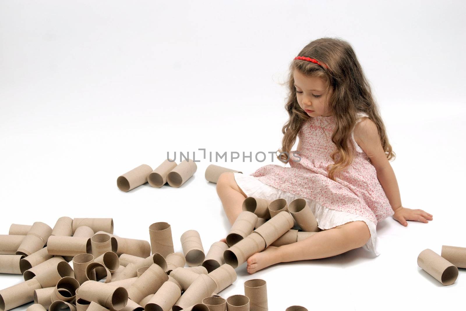 Little girl playing with lots of cardboard toilet paper rolls. White background