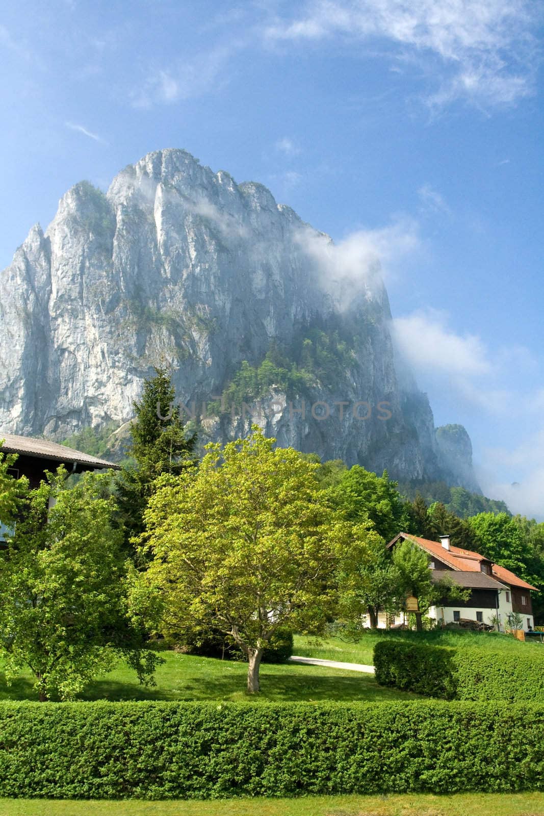 Tranquil spring countryside at the foot of foggy rock on the blue sky background