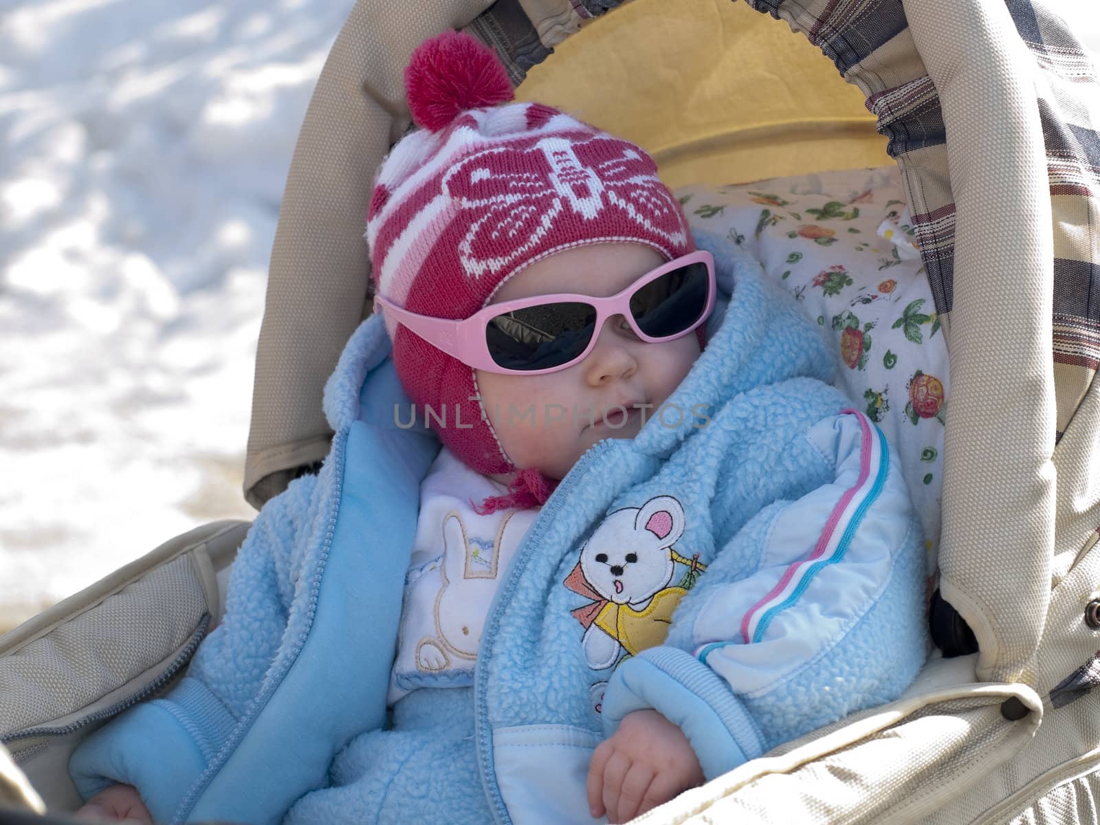 The small child in the dark glasses, sitting in a carriage.