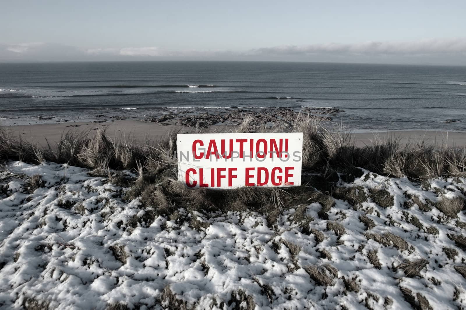 a red caution sign on a cliff edge in snow covered ballybunion