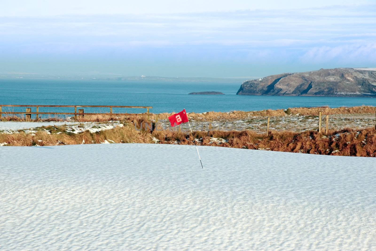 snow covering on a golf course in ireland in winter with sea and cliffs in background