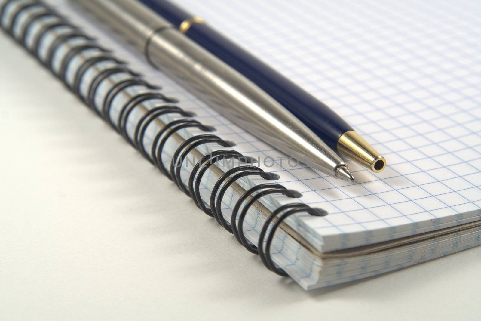 Two pens on spiral notebook on white background. Shallow depth of field
