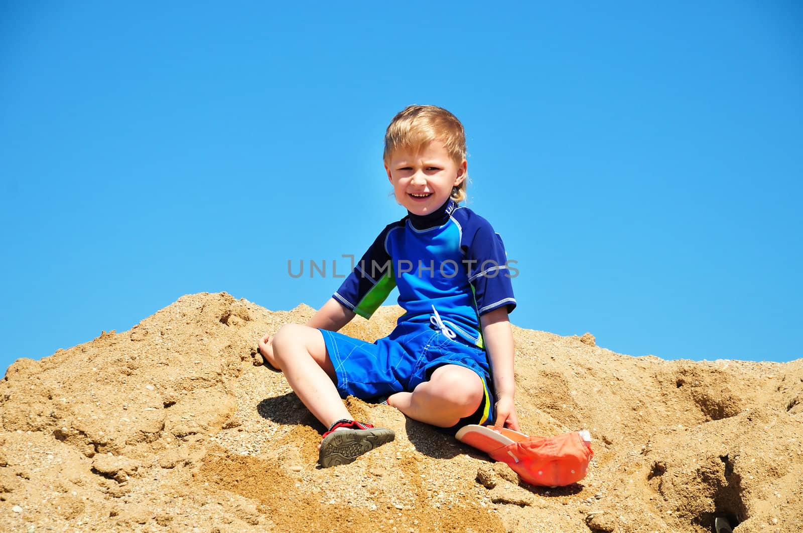 boy  wearing surf suit sitting in sand on the beach