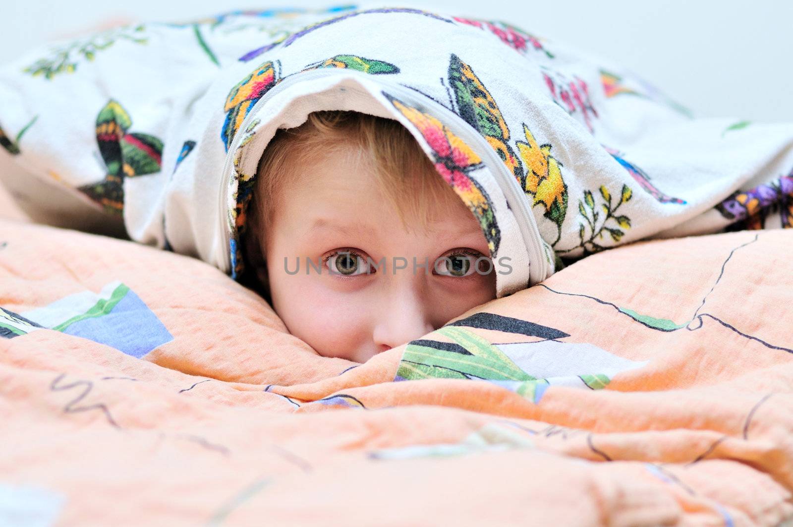 little boy laying under the pillow and watching something frightful on TV