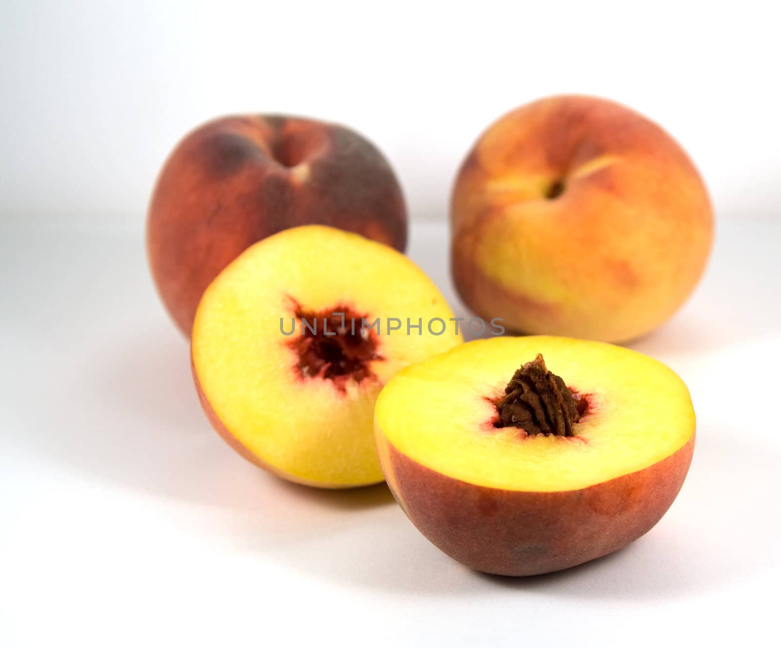 Half of peach with pit and two peaches on background