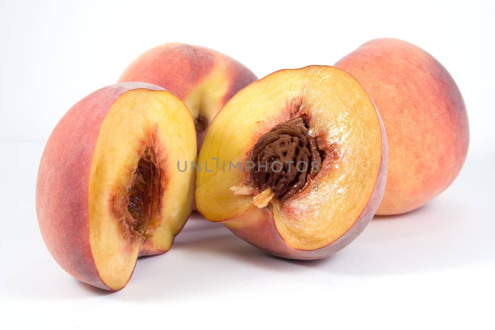 Three juicy peaches. Foreground one is divided in half by serpl
