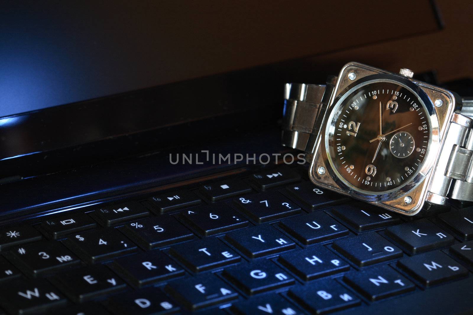 Closeup of steel wristwatch lying on black computer keyboard