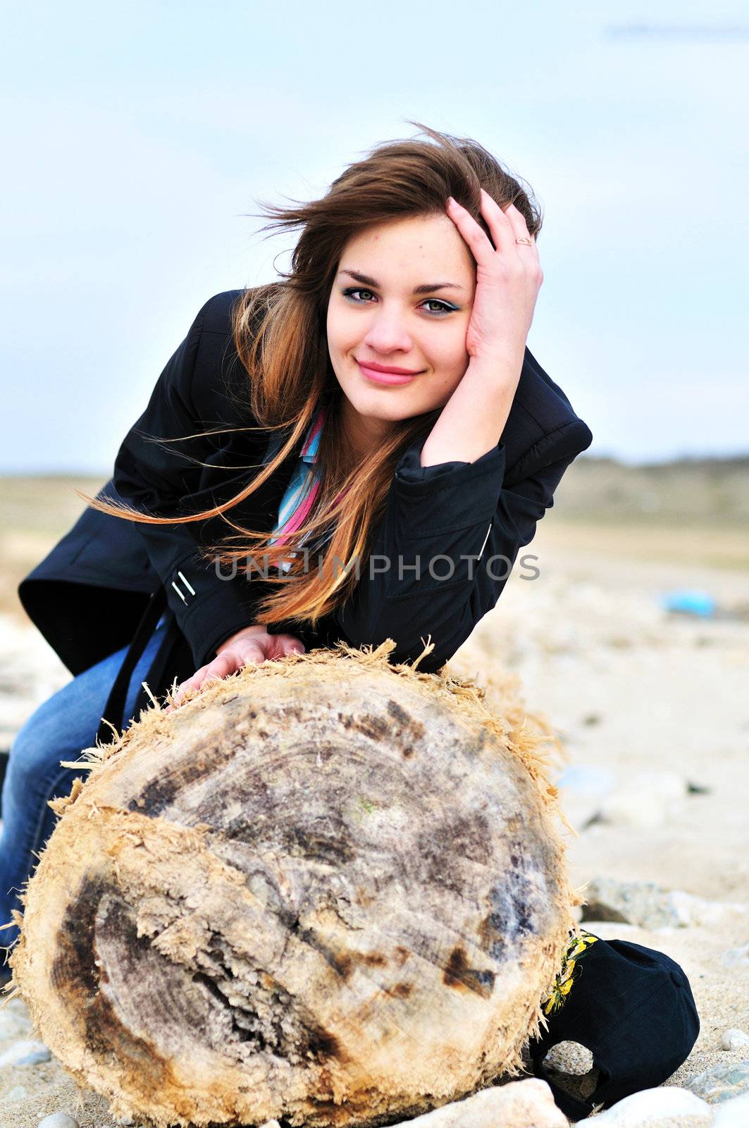 teen lovely girl on the beach sitting on the log
