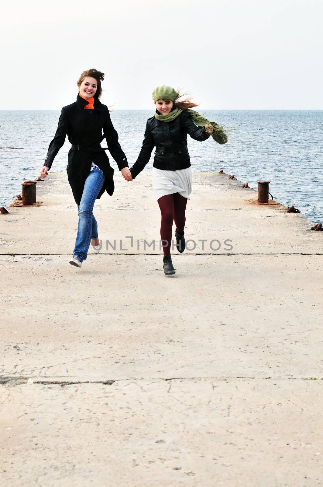 two happy running girls on the dock near the sea