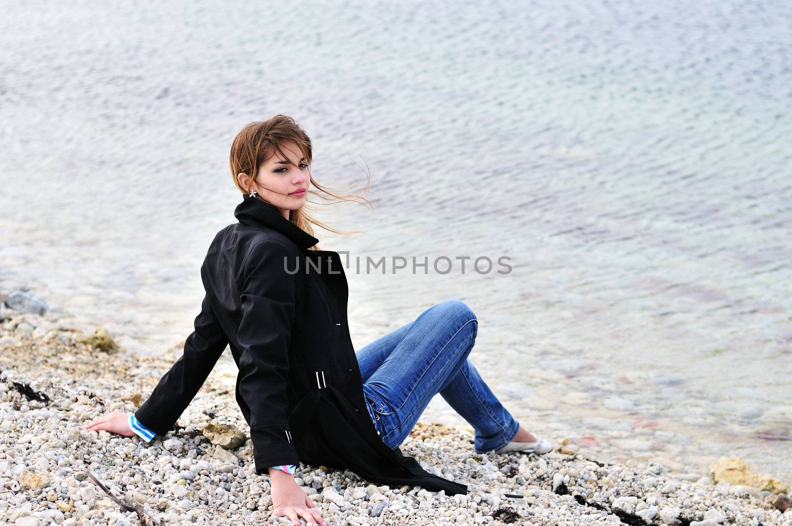  lovely teen girl sitting on the pebble close to sea in spring time
