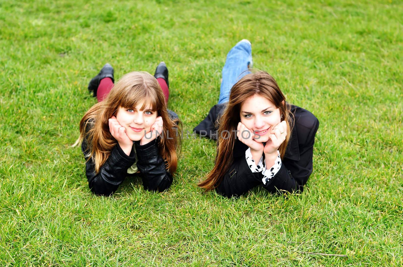 teen girls laying on the green grass by Reana
