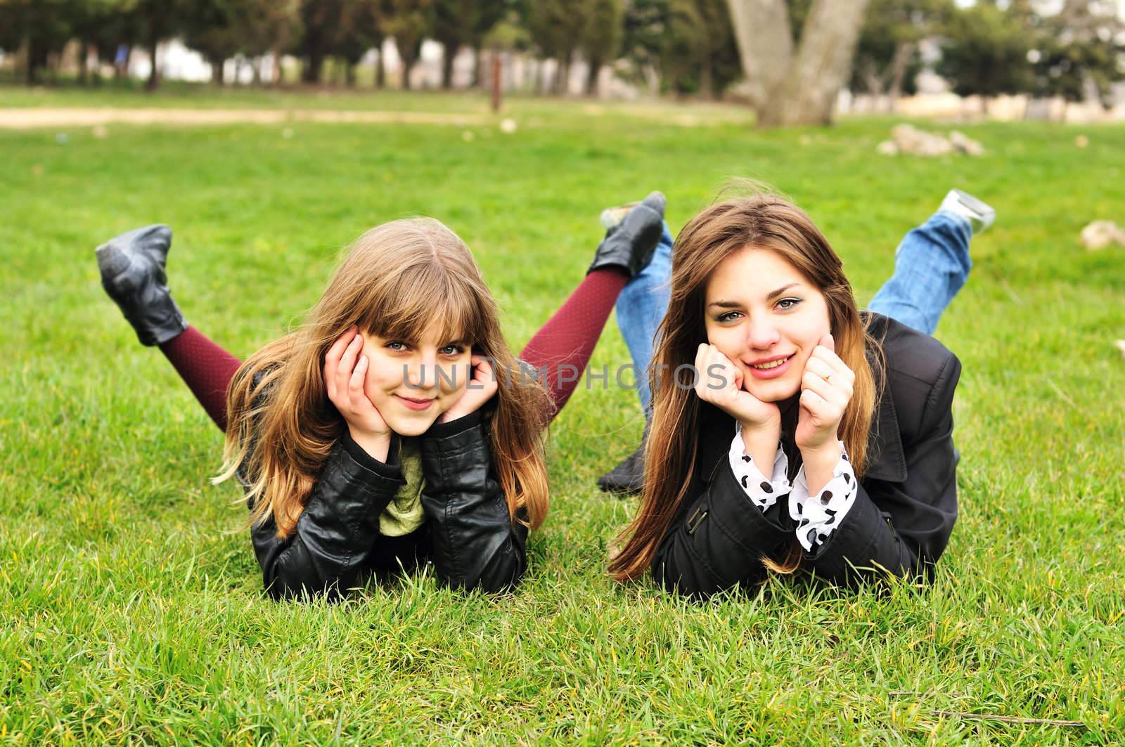  two funny teen girls laying on the green grass
