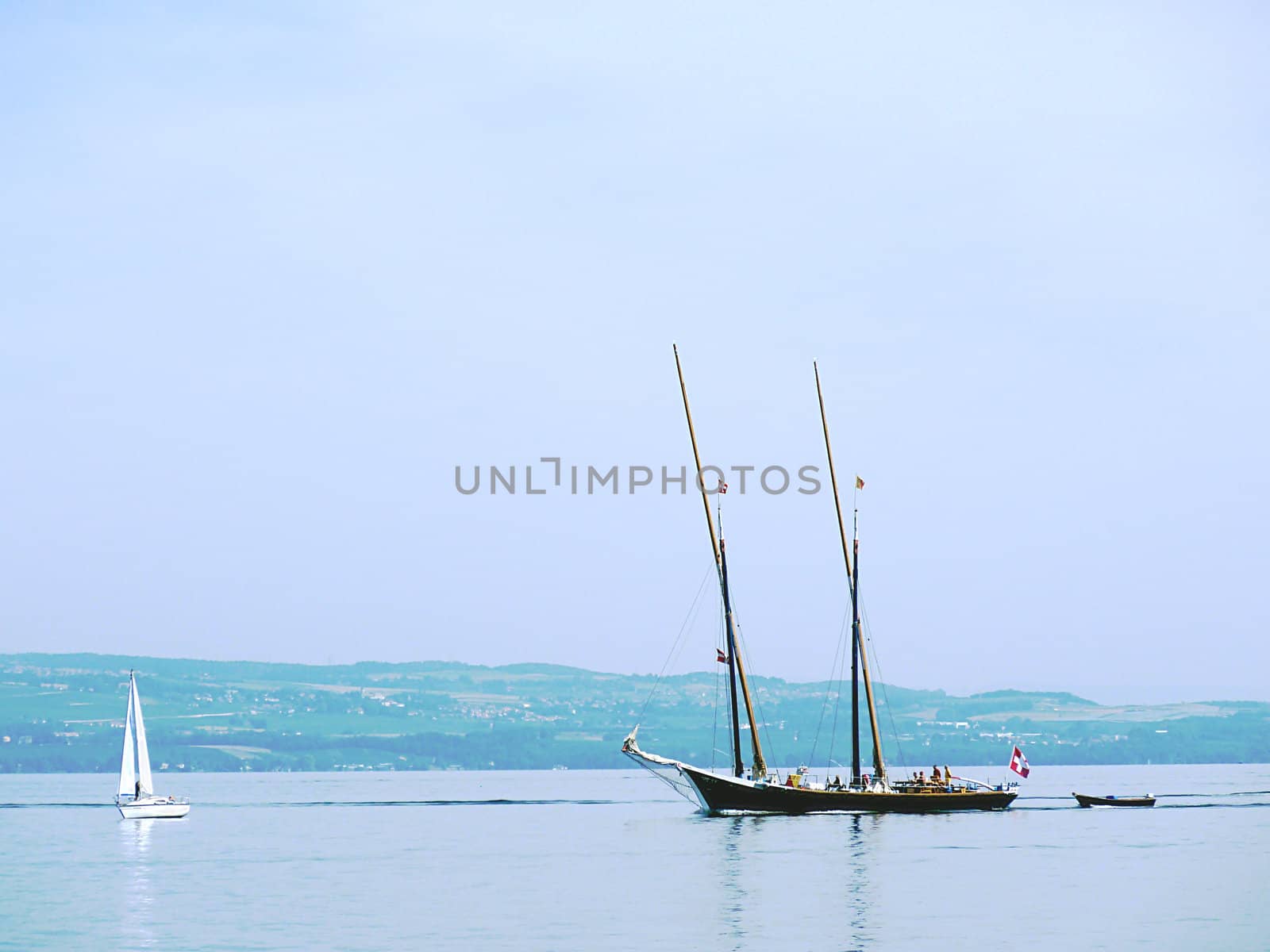 Big ancient boat and small white sailing boat on lake of Geneva, Switzerland, with little hill behind
