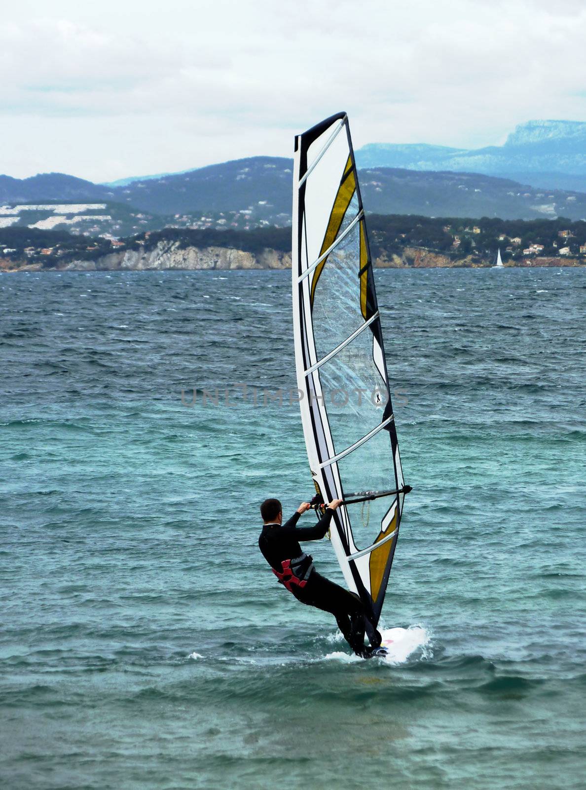 Suited windsurfer on mediterranean french coastline by cold weather