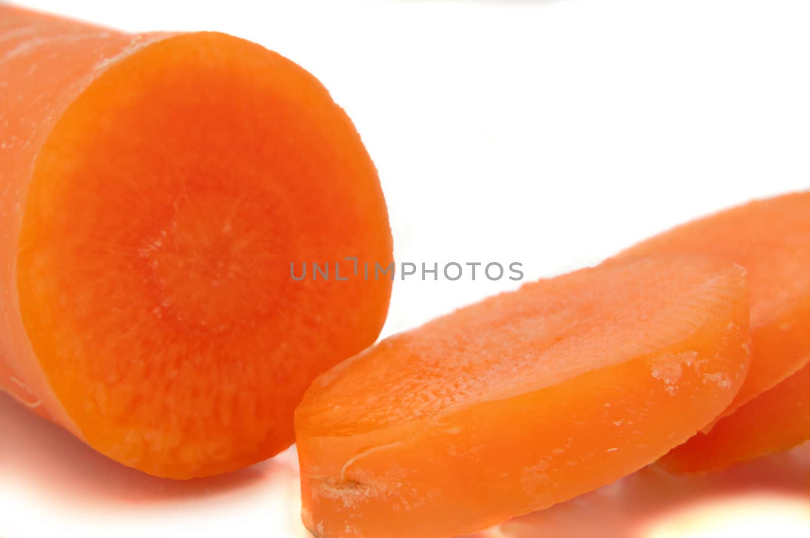 Close and low level of a partially sliced carrot arranged over white.