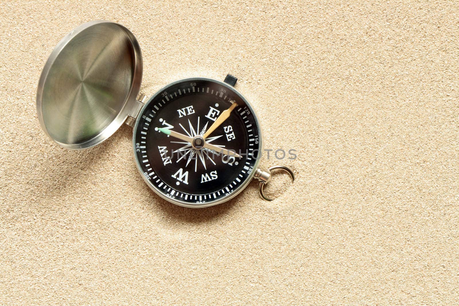 Closeup of open compass lying on yellow sand background with copy space