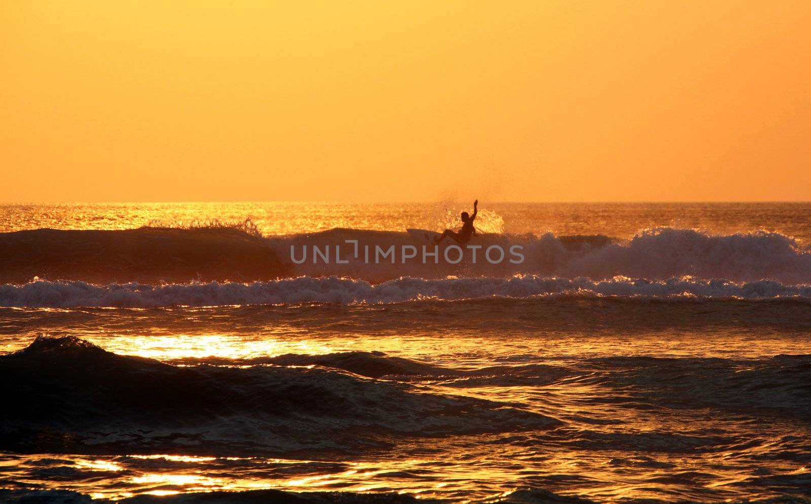 Surfer rides waves at sunset, Bali, Indonesia