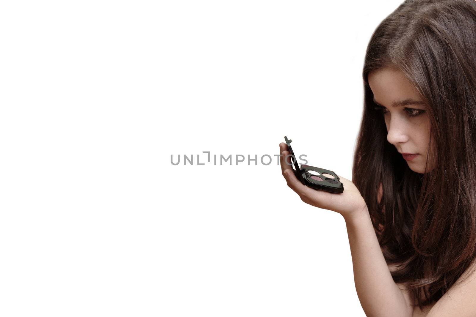 A beautiful brown haired  young girl holding makeup box and looking to the mirror, isolated over white background