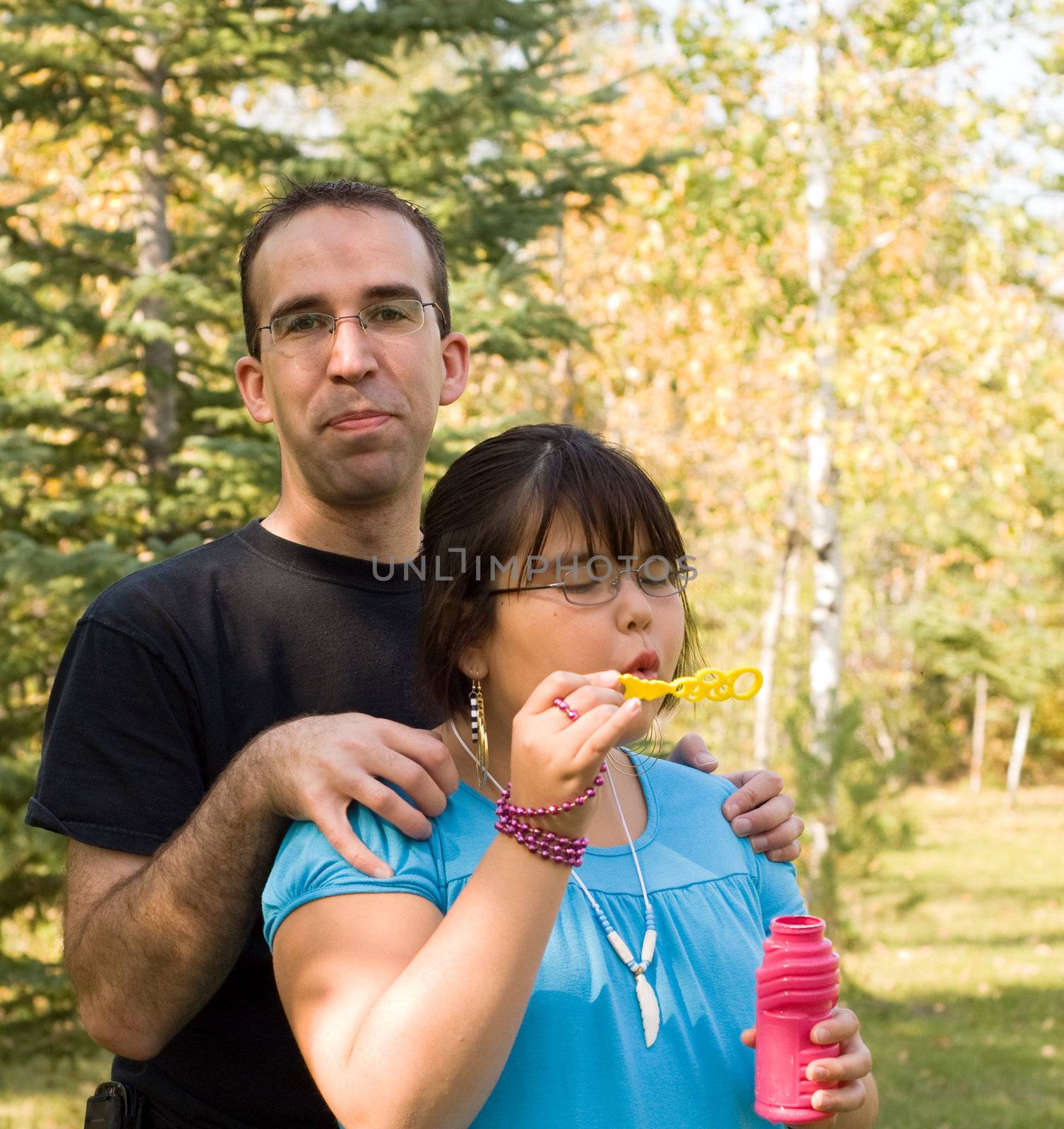 A young father standing behind his bubble blowing daughter