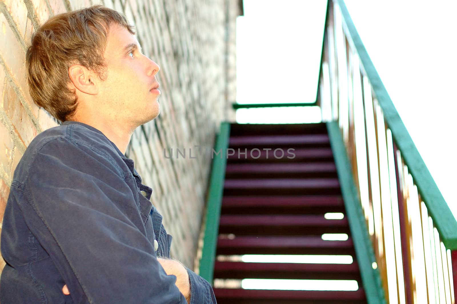 Young stylish man with blonde hair stand near brick wall and stairs.