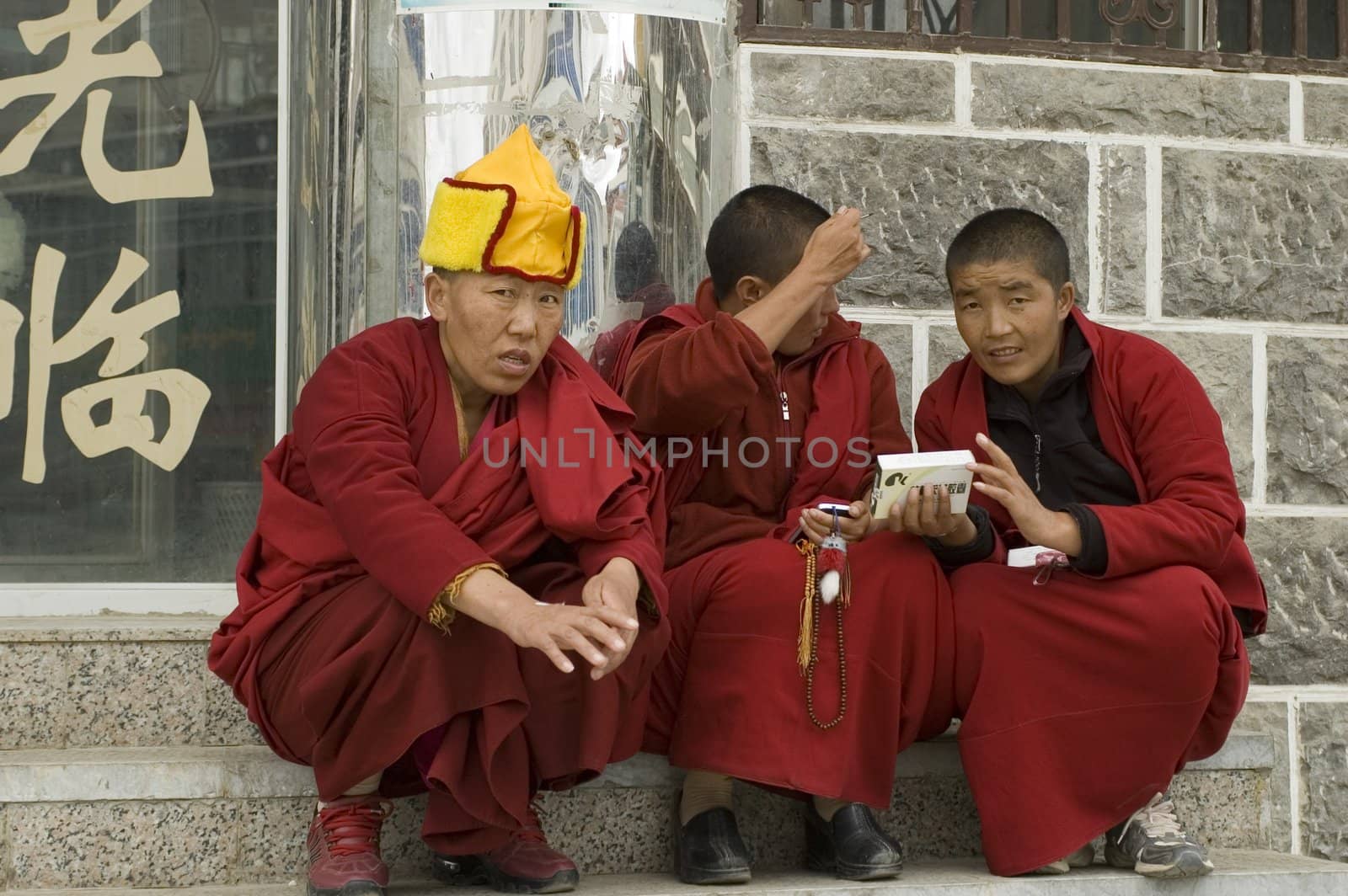 CHINA, YUNNAN PROVINCE, SHANGRILA CITY - SEPTEMBER 13: Three Tibetan monks sitting in front of shop, wearing traditional clothes.