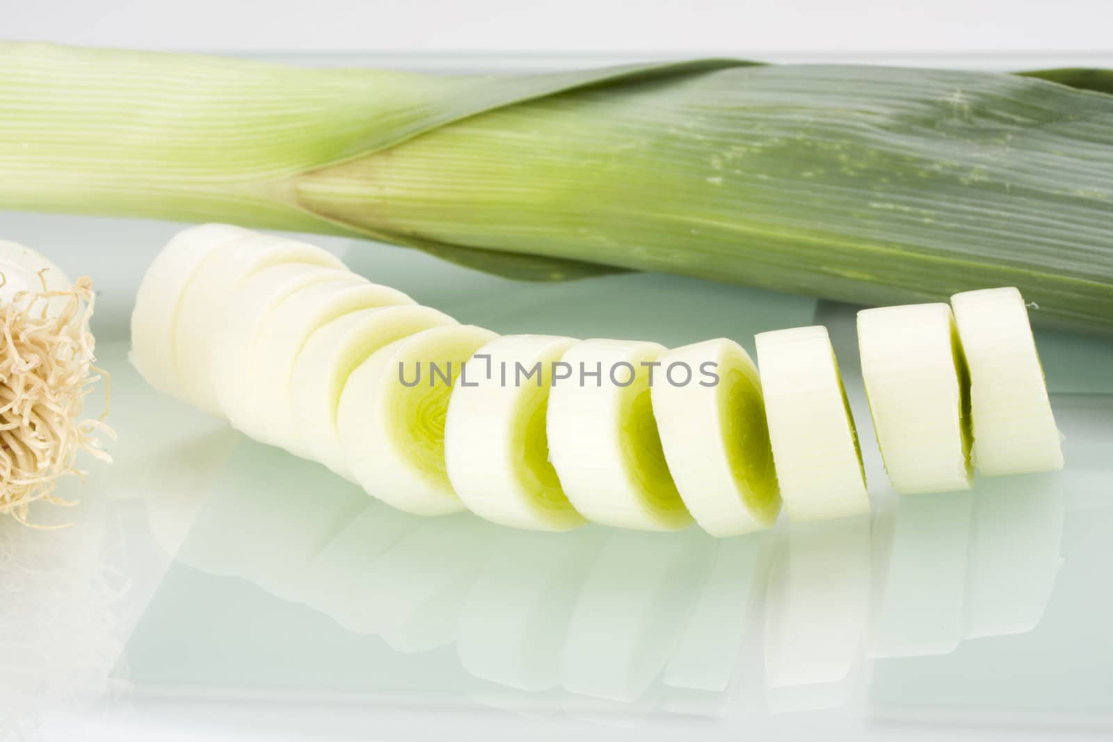 slices of leek on a glass chopping board by bernjuer