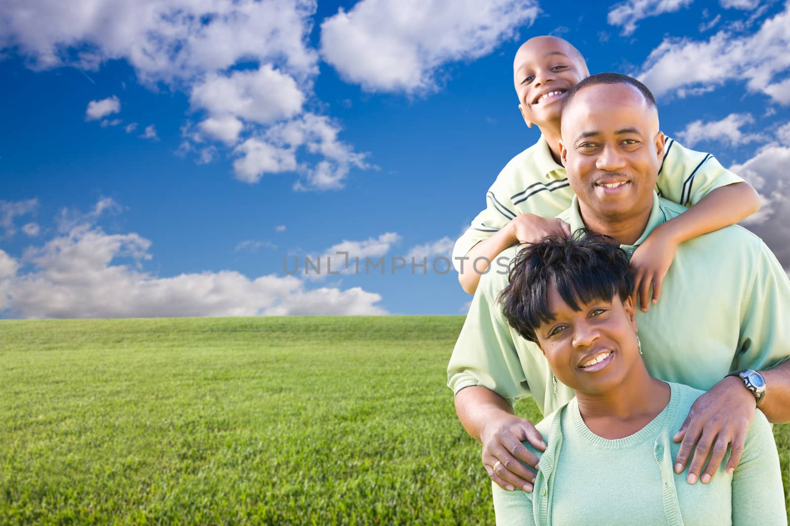 Happy African American Family Over Grass Field, Clouds and Blue Sky - Room For Your Own Text to the Left.