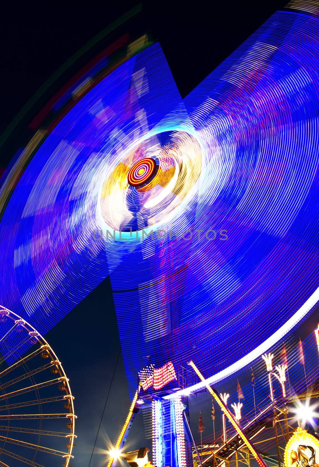 fast merry-go-round by night with great lights and ferris wheel in background