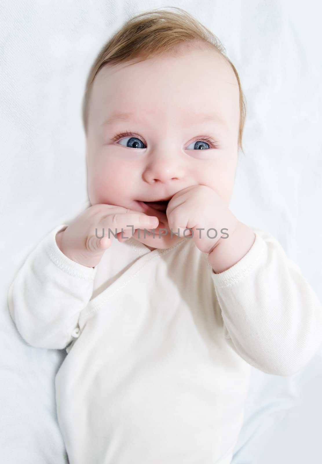 Adorable laughing baby boy lying with hands in his mouth