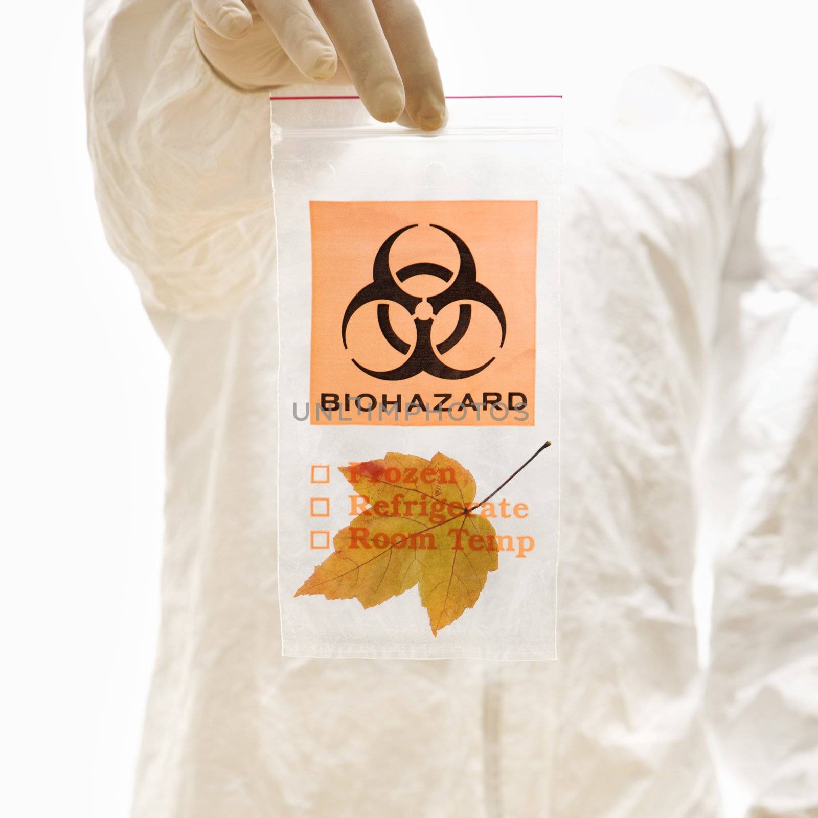 Man in biohazard suit and rubber gloves holding plastic biohazard bag containing orange Maple leaf.