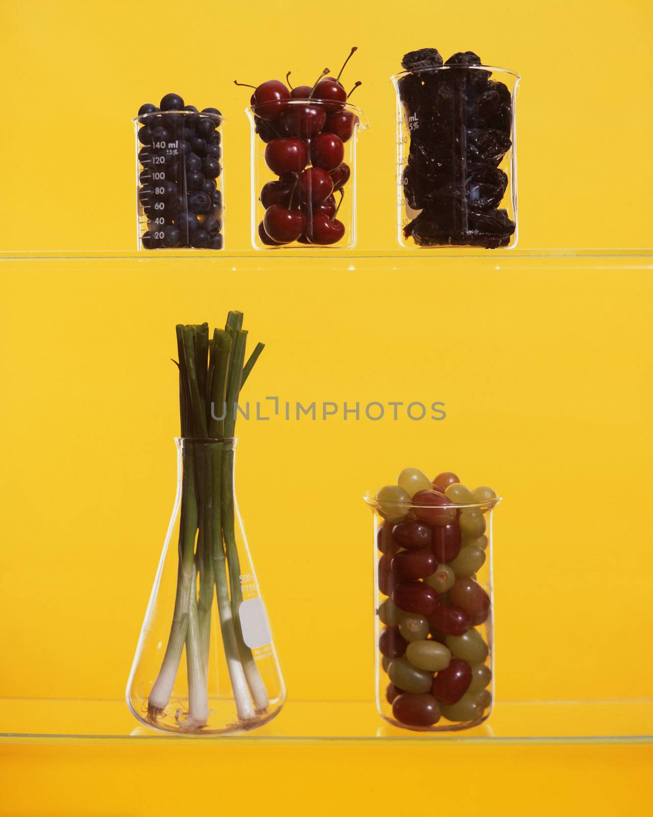Beakers and flask filled with fruit and onions on yellow background
