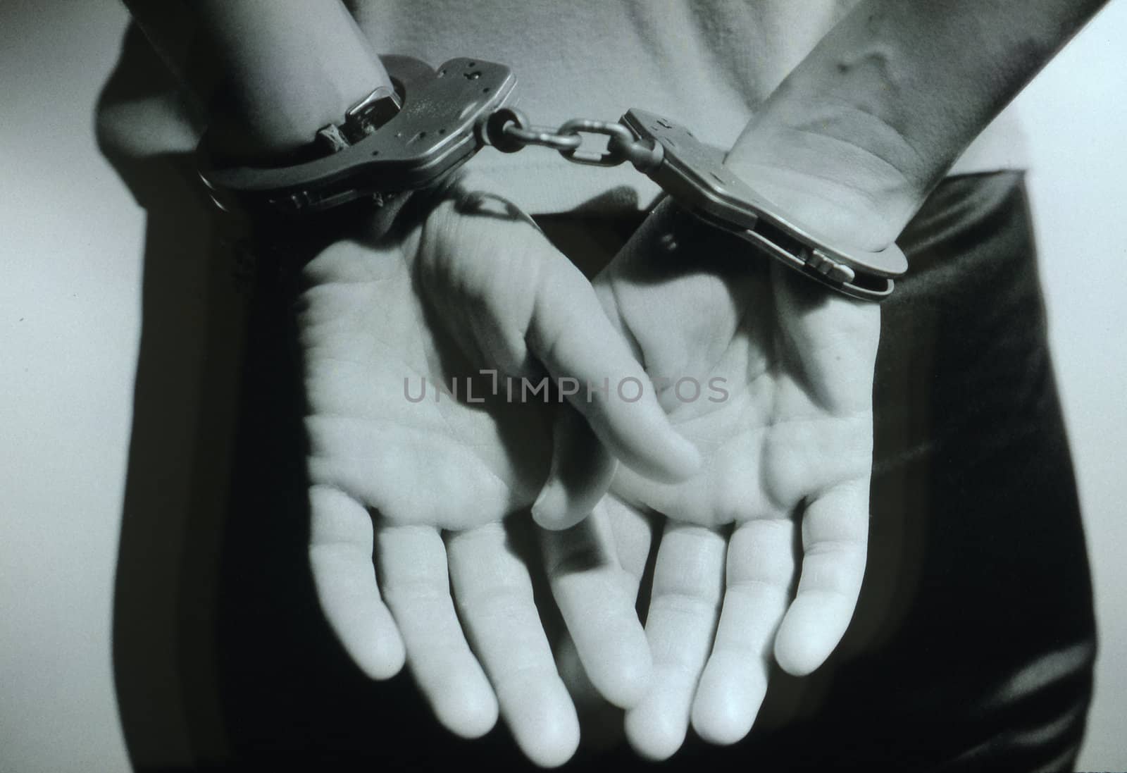 A black and white photo of woman's hands in cuffs behind her
