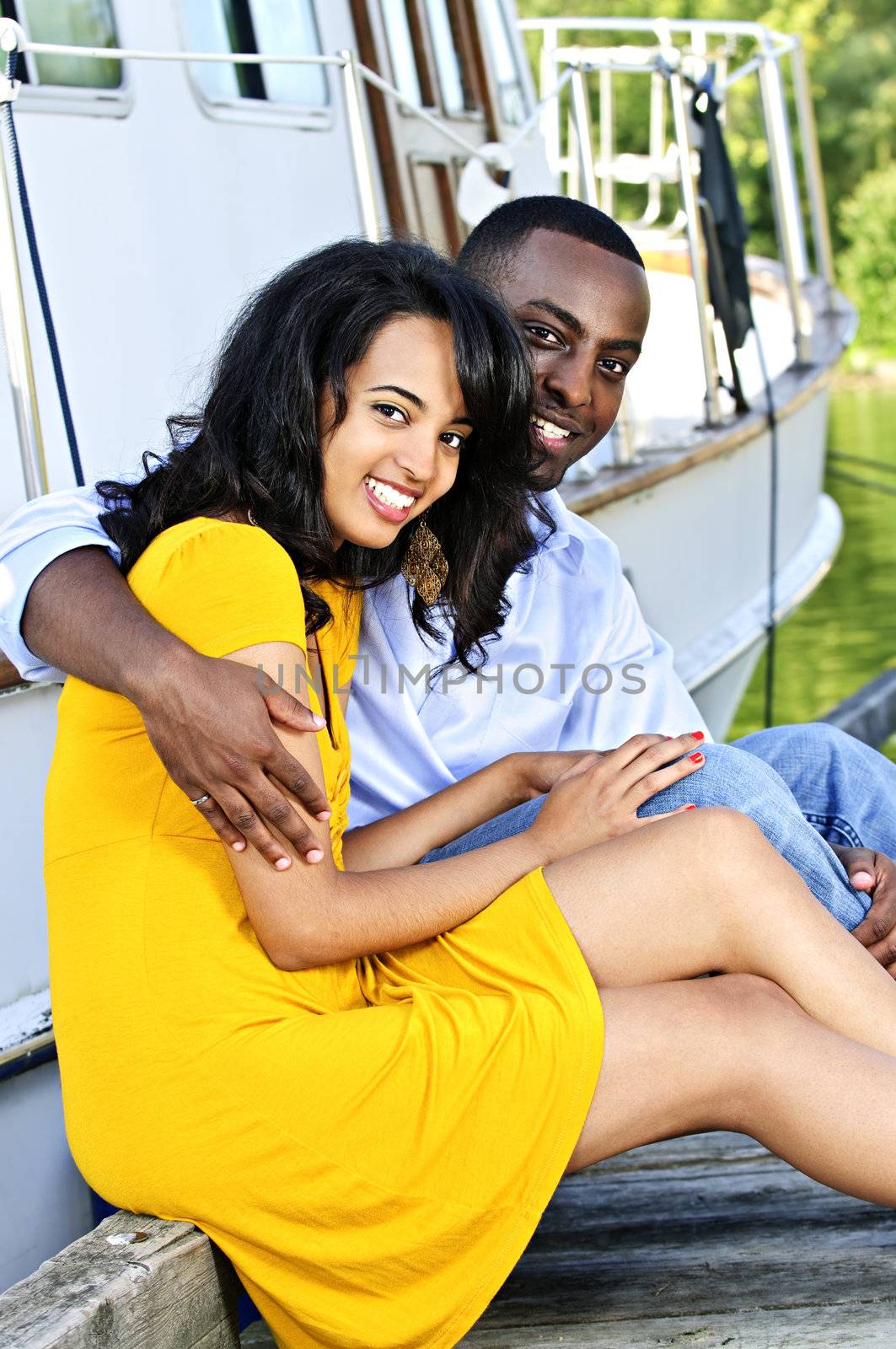 Young romantic couple sitting on dock in front of yacht