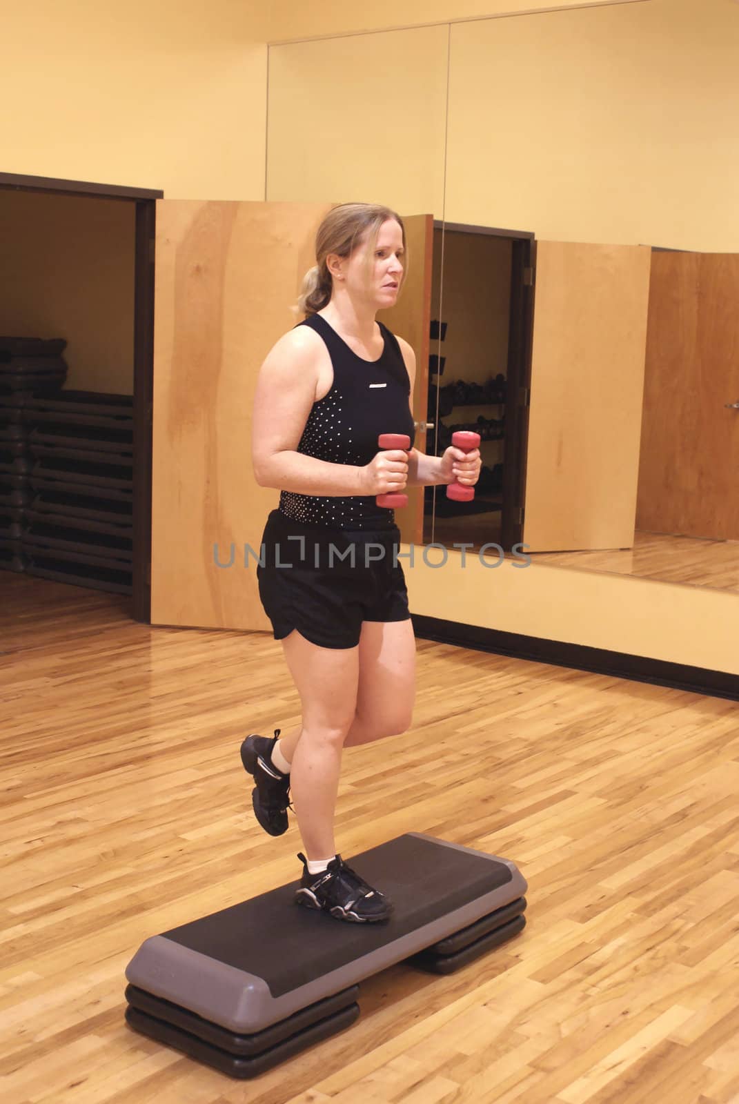 Woman working out in a gym using hand weights and a step.              