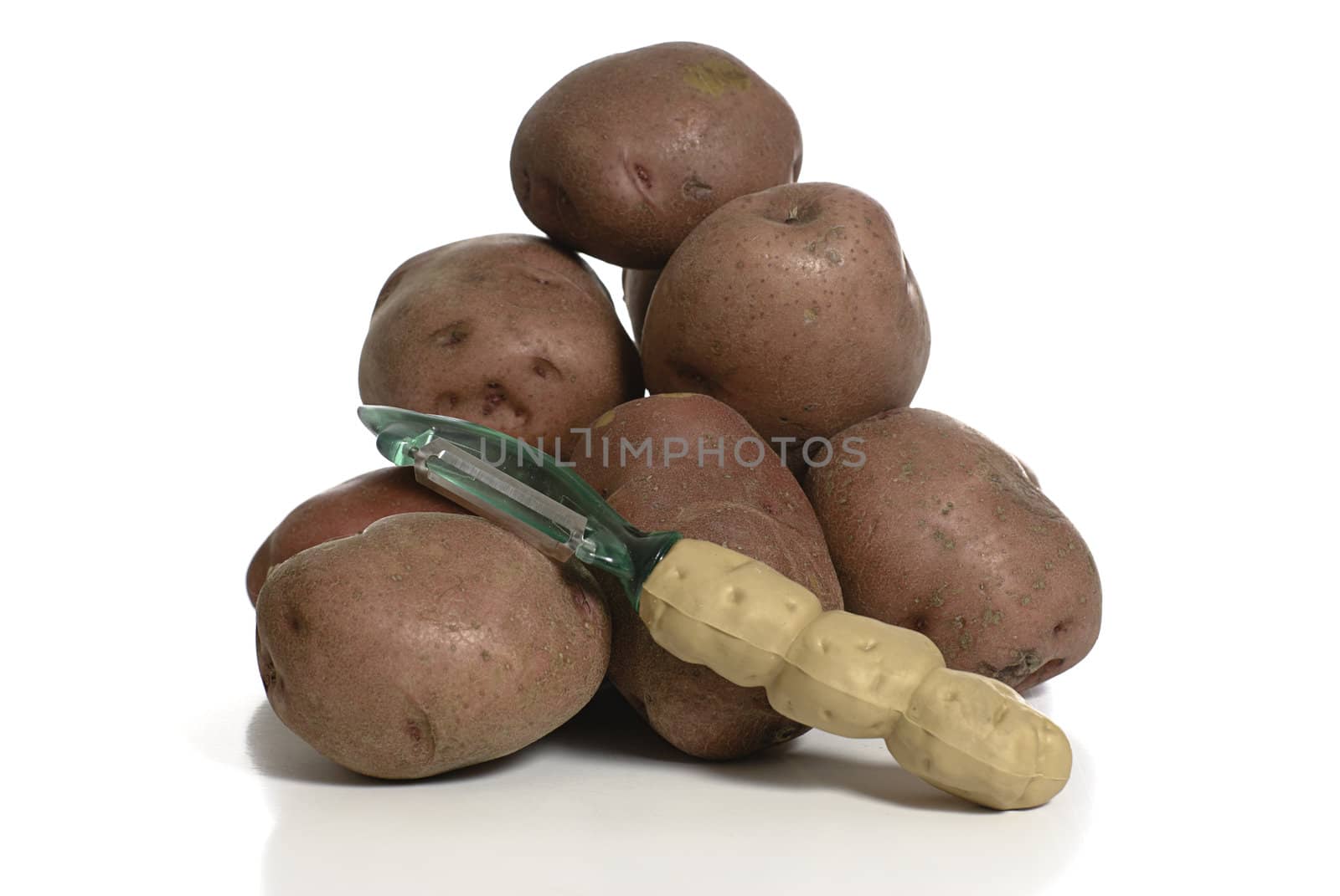 A potato peeler ready to be used on this pile of organic red potatoes, shot on a white background, with a reflection