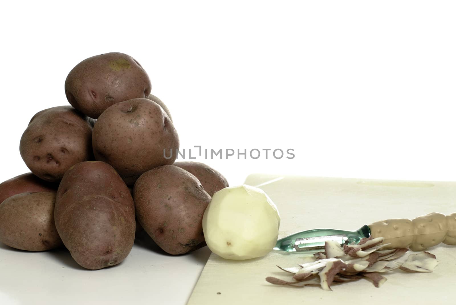 Peeled and unpeeled potatoes shot on a cutting board, isolated against a white background.