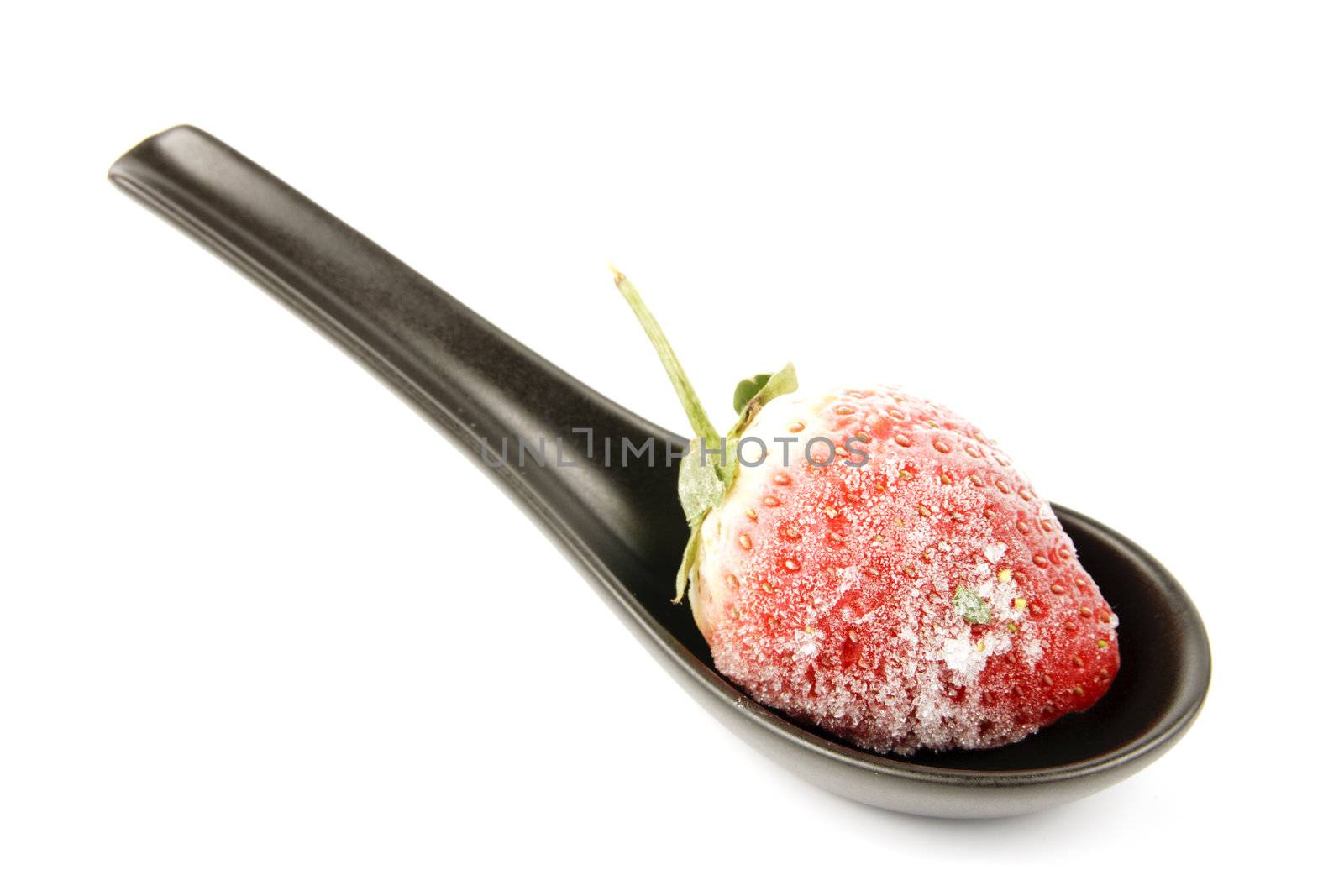 Red ripe frozen strawberry on a small black spoon with a reflective white background