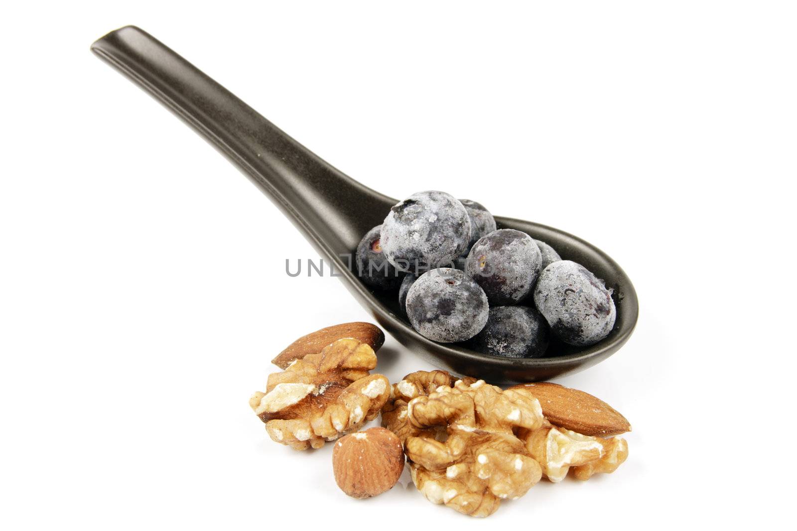Blue ripe blueberries on a small black spoon with mixed nuts on a reflective white background