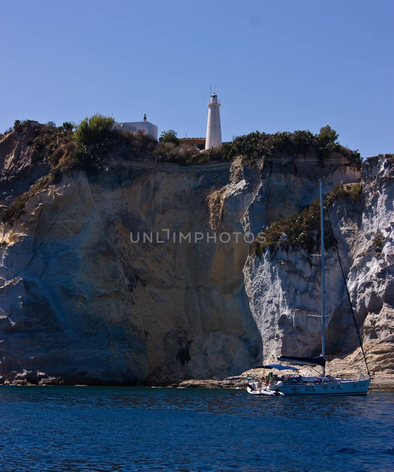 Lighthouse on steep mountain and sail yacht near Ponza island (Italy).