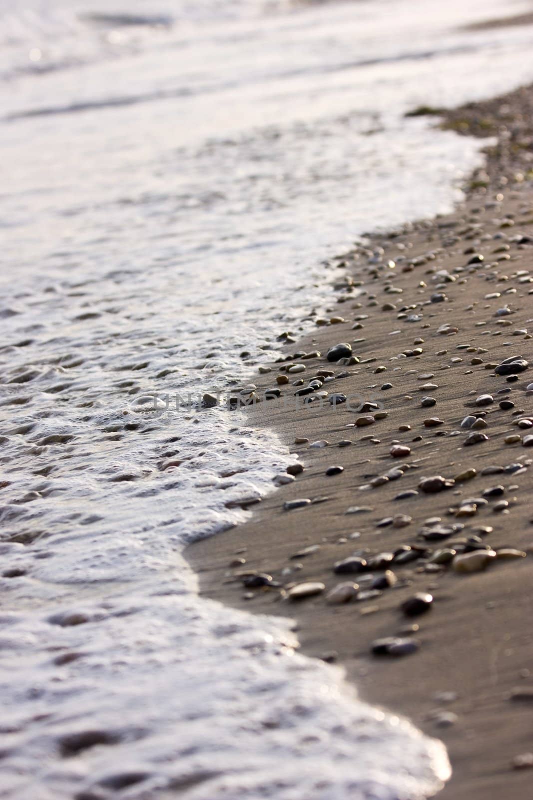 Coastline covered with pebbles with blurred waves and spindrift