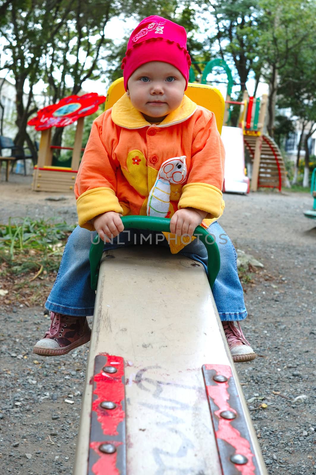 Pretty little girl with bright jacket sit on seesaw (teeter-totter).