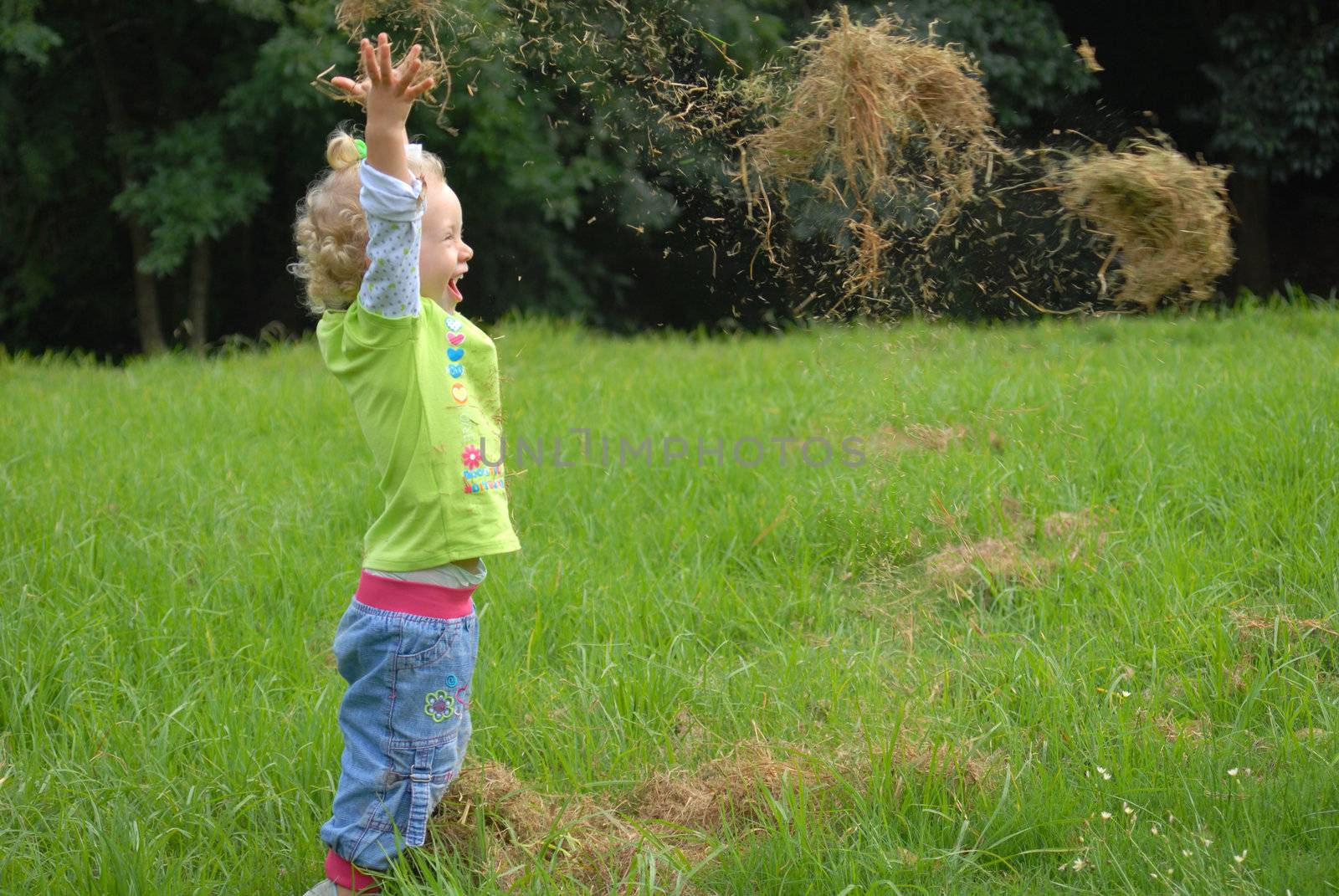 Blondie girl playing with grass on the green field.