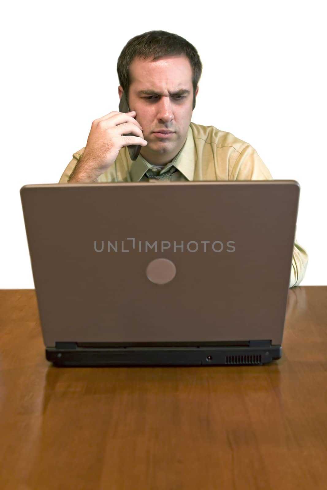 A man working from home with his cell phone and laptop. He has an upset or serious look on his face.