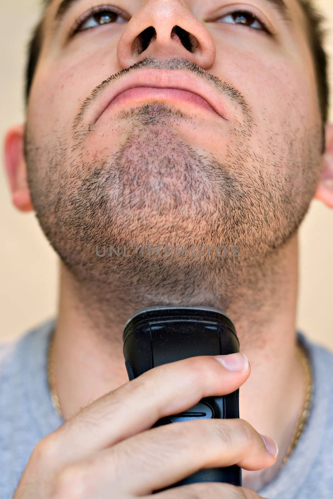 A closeup of a young man shaving his beard off with an electric shaver.