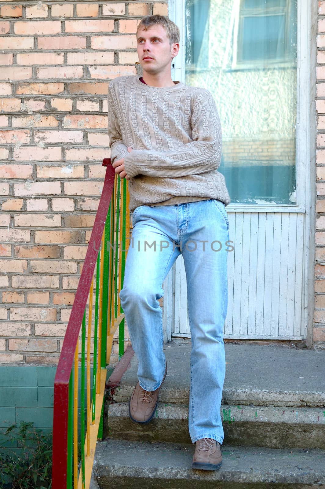 Young stylish man with blonde hair stay on stairs near brick wall.