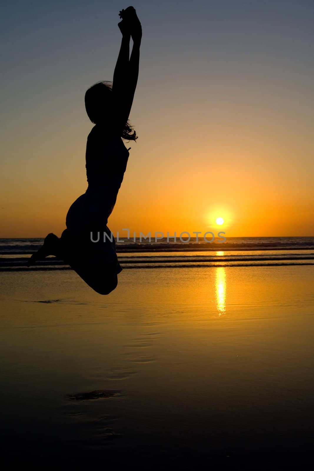 Woman jumping on the beach at sunset.