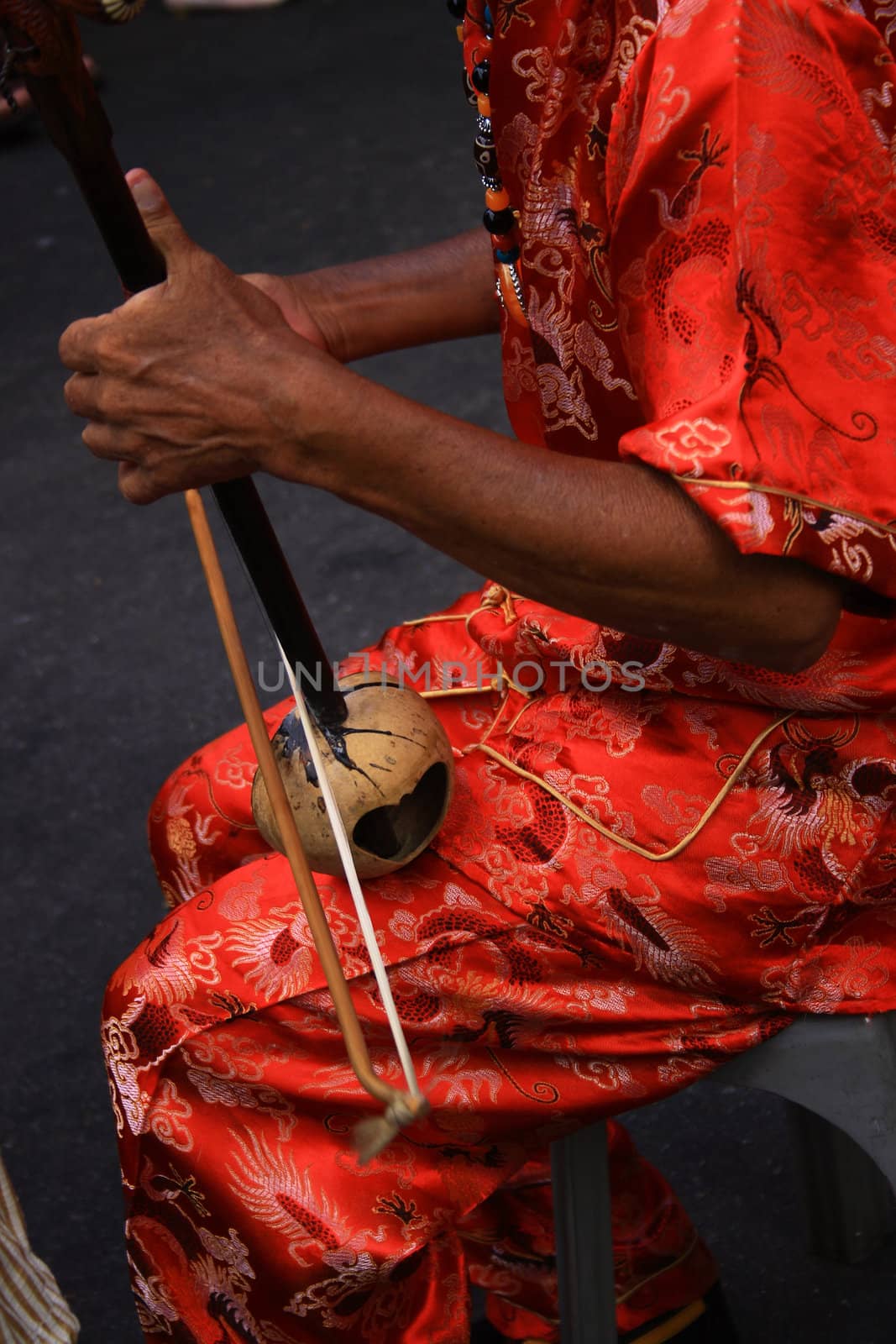 An old man wearing in red playing a Chinese instrument, er wu.